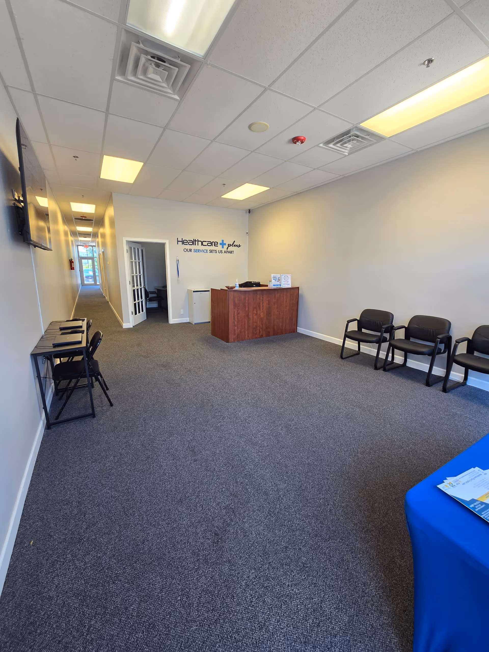 Reception area with a wooden desk, row of black chairs, and hallway at Healthcare Plus Caregivers.