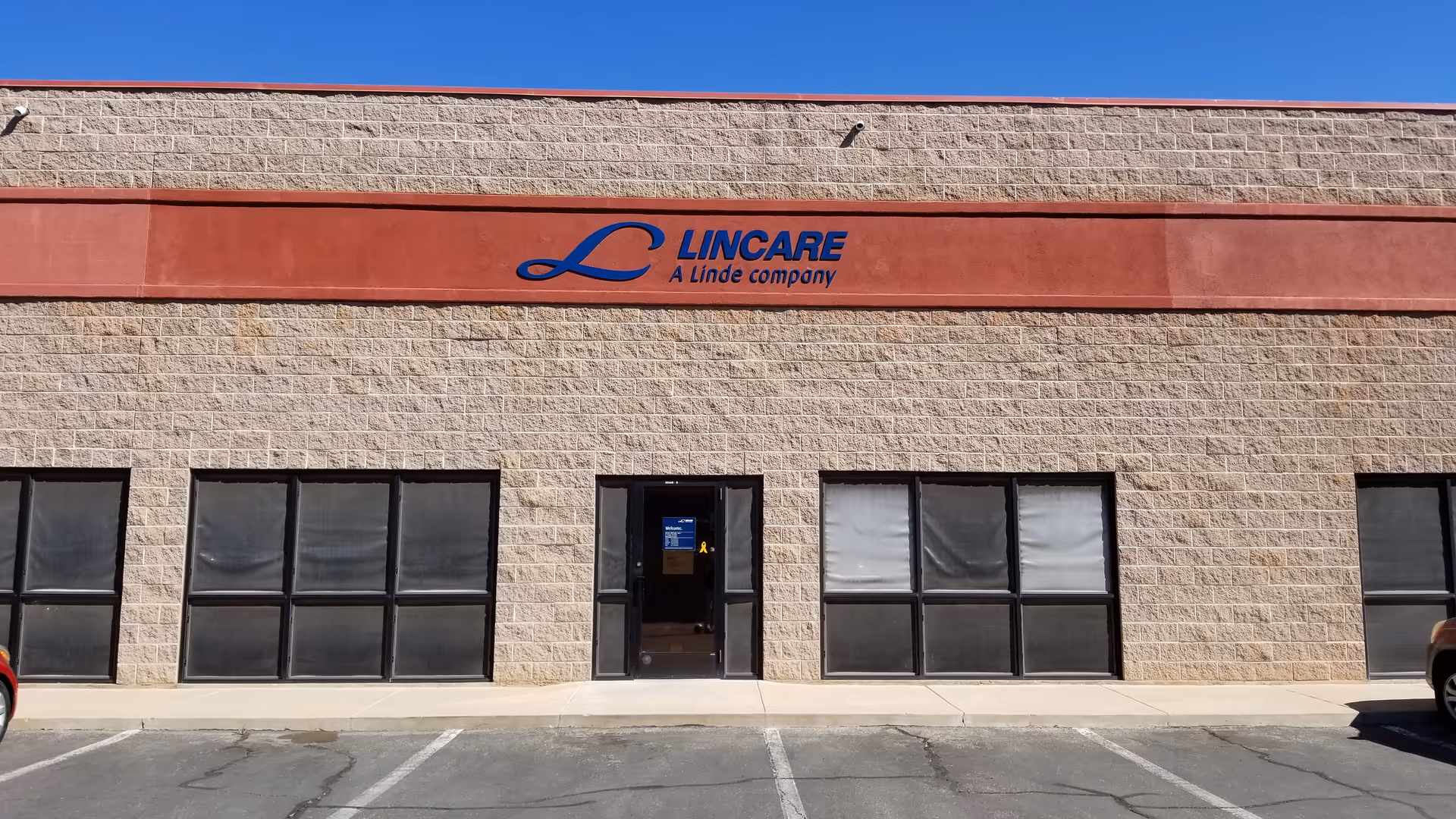 Large beige brick building with a red sign and LINCARE logo outside, no people.