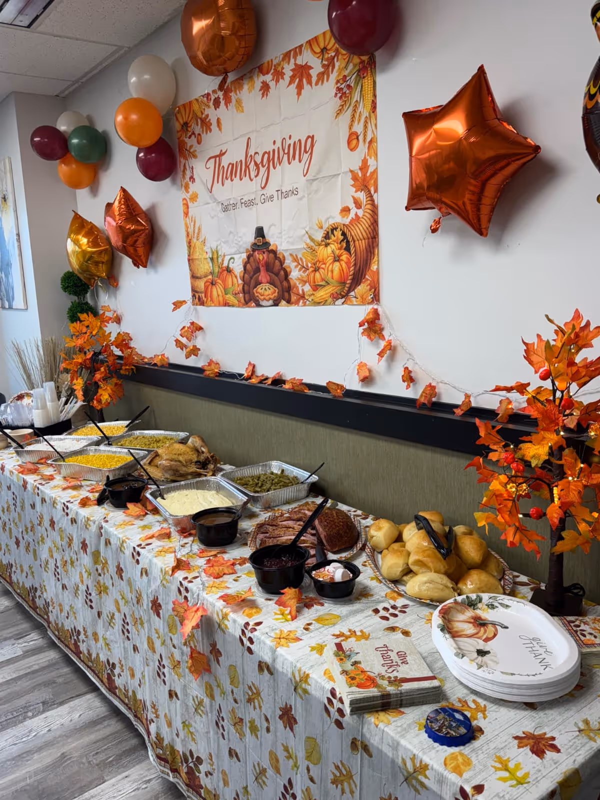Indoor Thanksgiving buffet with autumn decorations and assorted dishes on a long table.