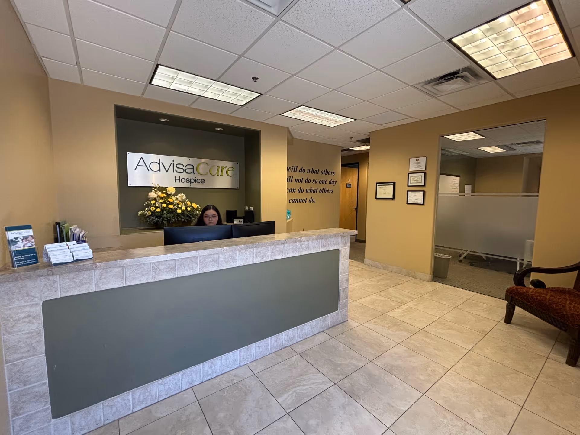 Reception desk in a beige hospice lobby with staff, flowers, and frosted partition walls