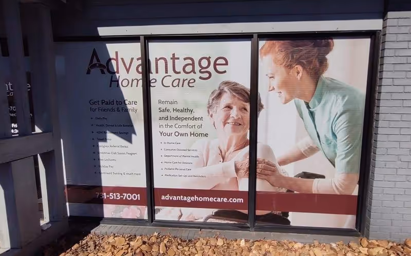Storefront windows display Advantage Home Care branding with a caregiver and elderly woman.