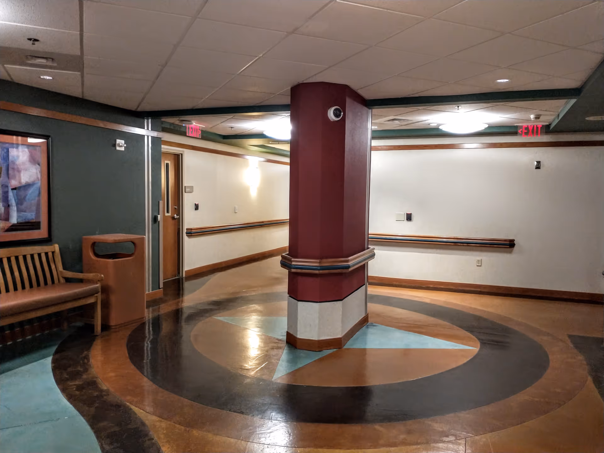 Interior hallway of a senior facility with a central maroon pillar and circular floor pattern.