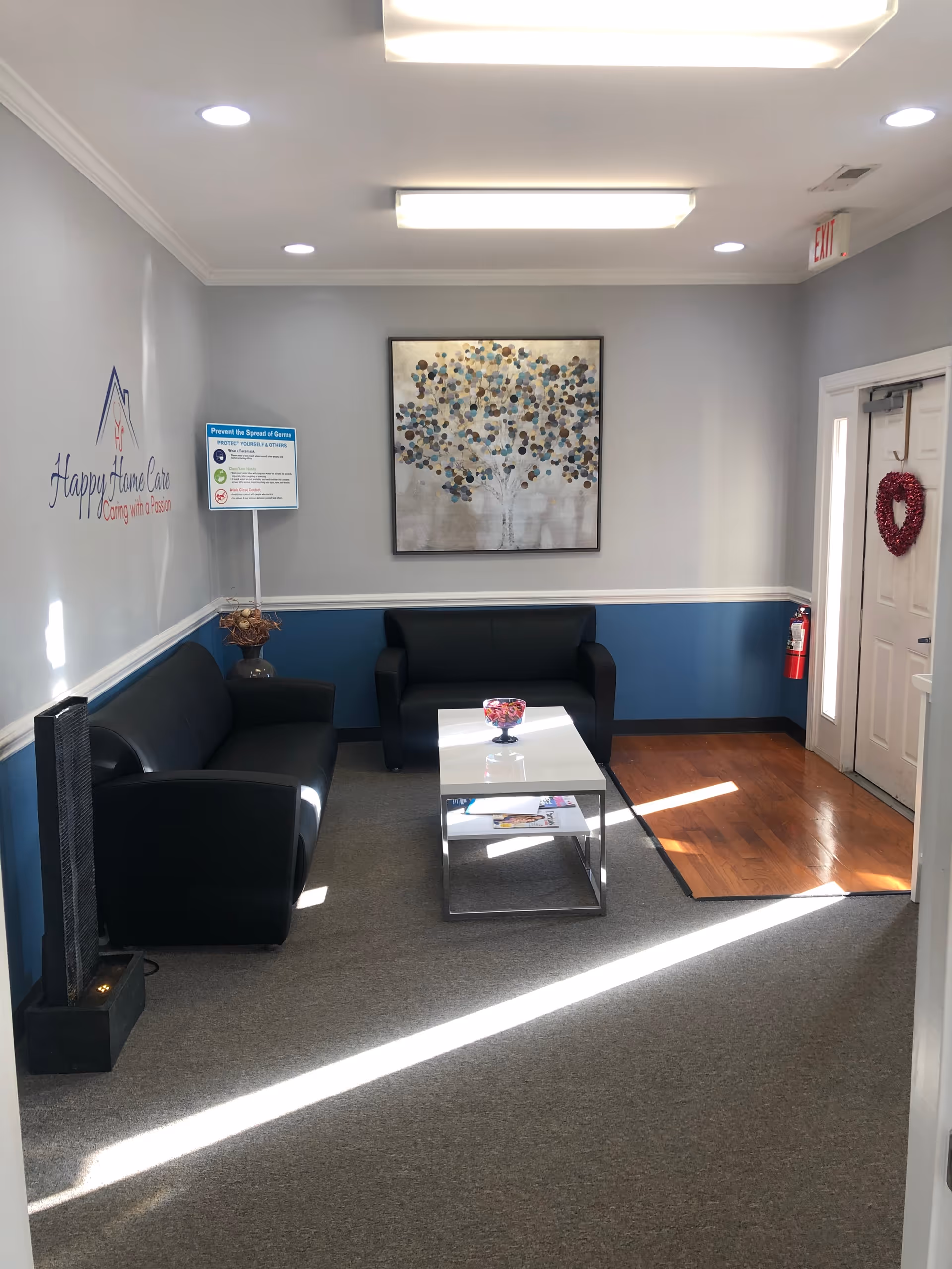 Modern lobby lounge with black leather sofas, glass coffee table, wall art, and door.