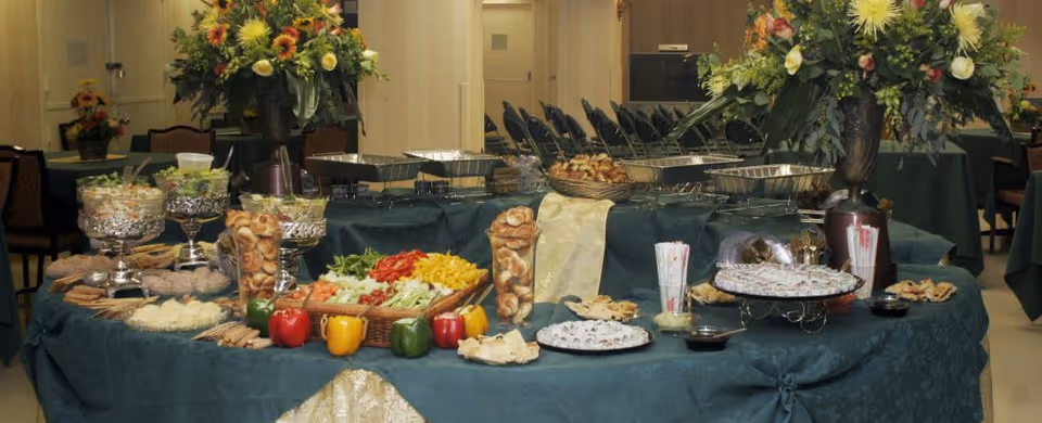 Buffet table with assorted foods and large floral arrangements in a dining room.