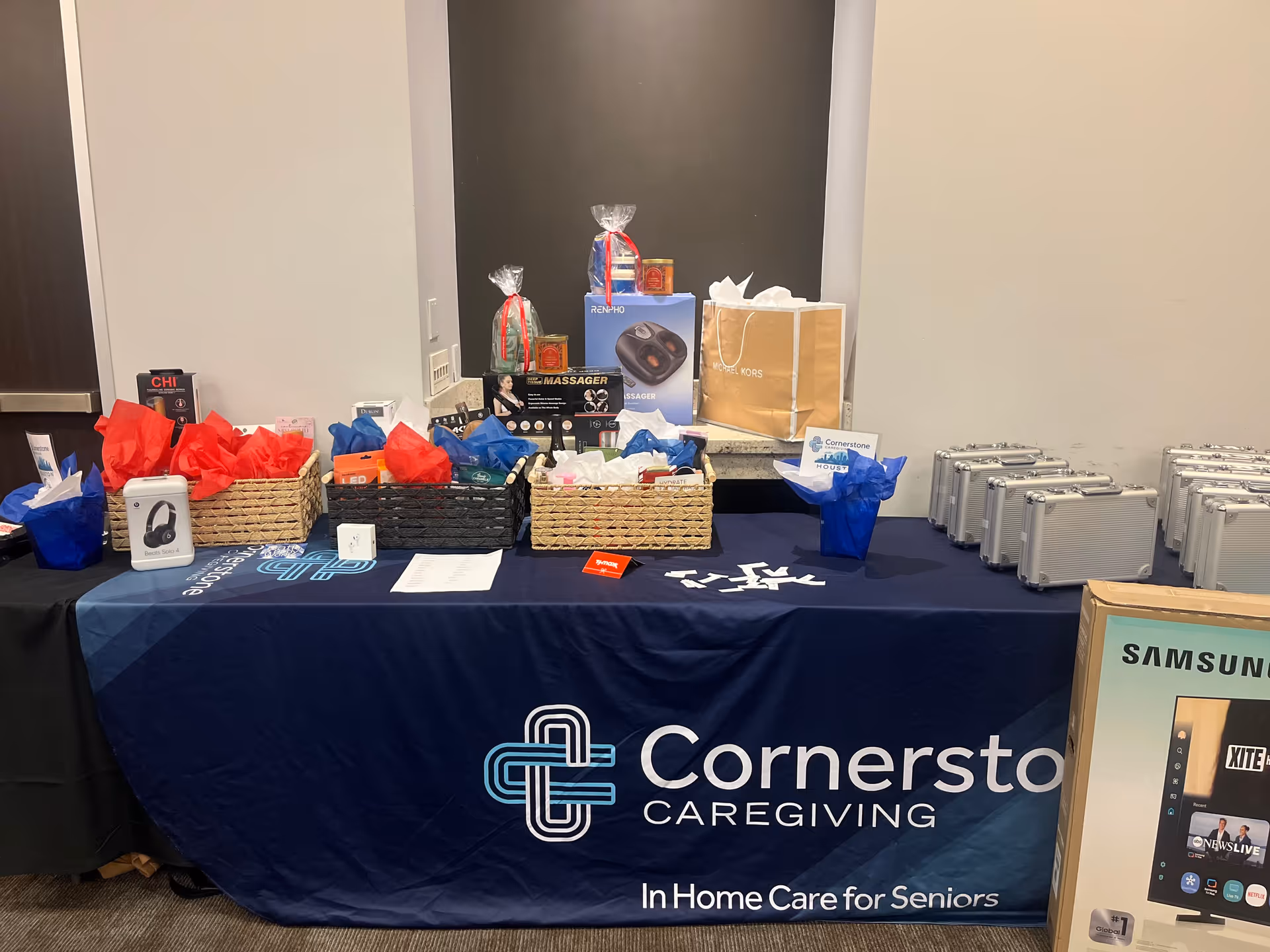 Indoor display table with Cornerstone Caregiving banner, gift baskets, and prize boxes.