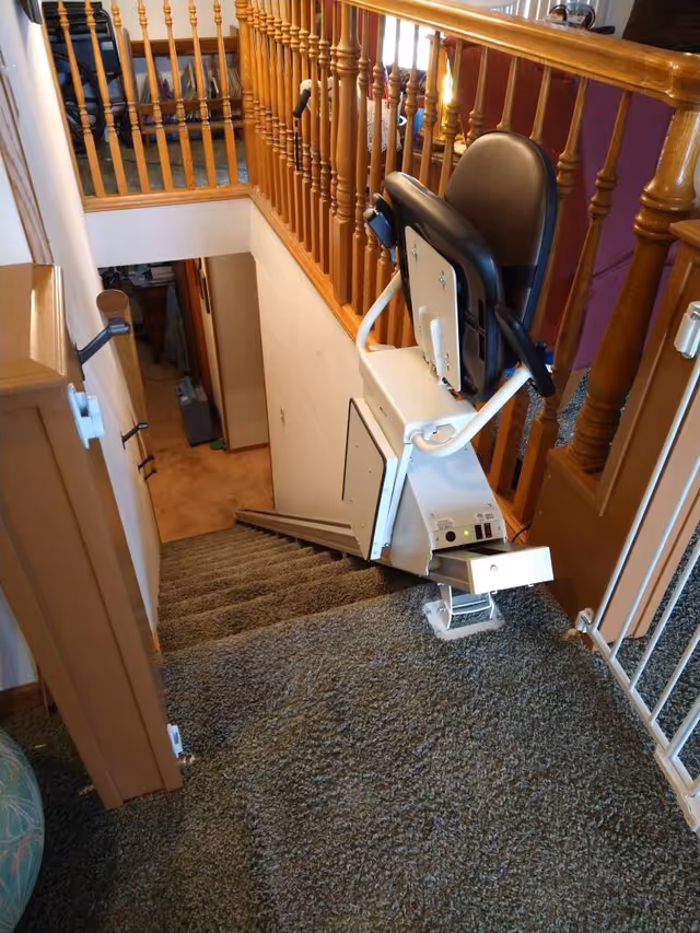 Indoor stairwell with a mounted chairlift for accessibility on carpeted stairs.