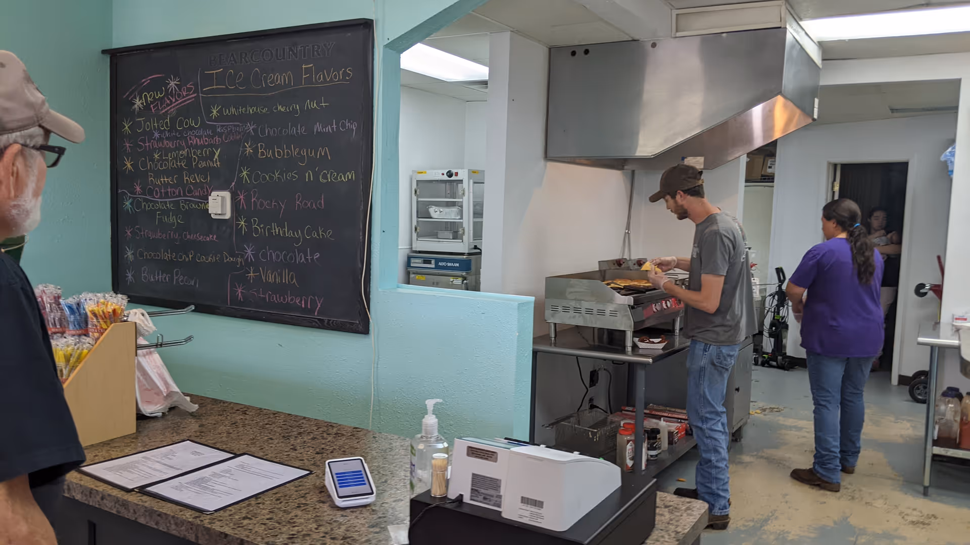 A kitchen area in a senior facility with a grill, chalkboard menu, and staff.