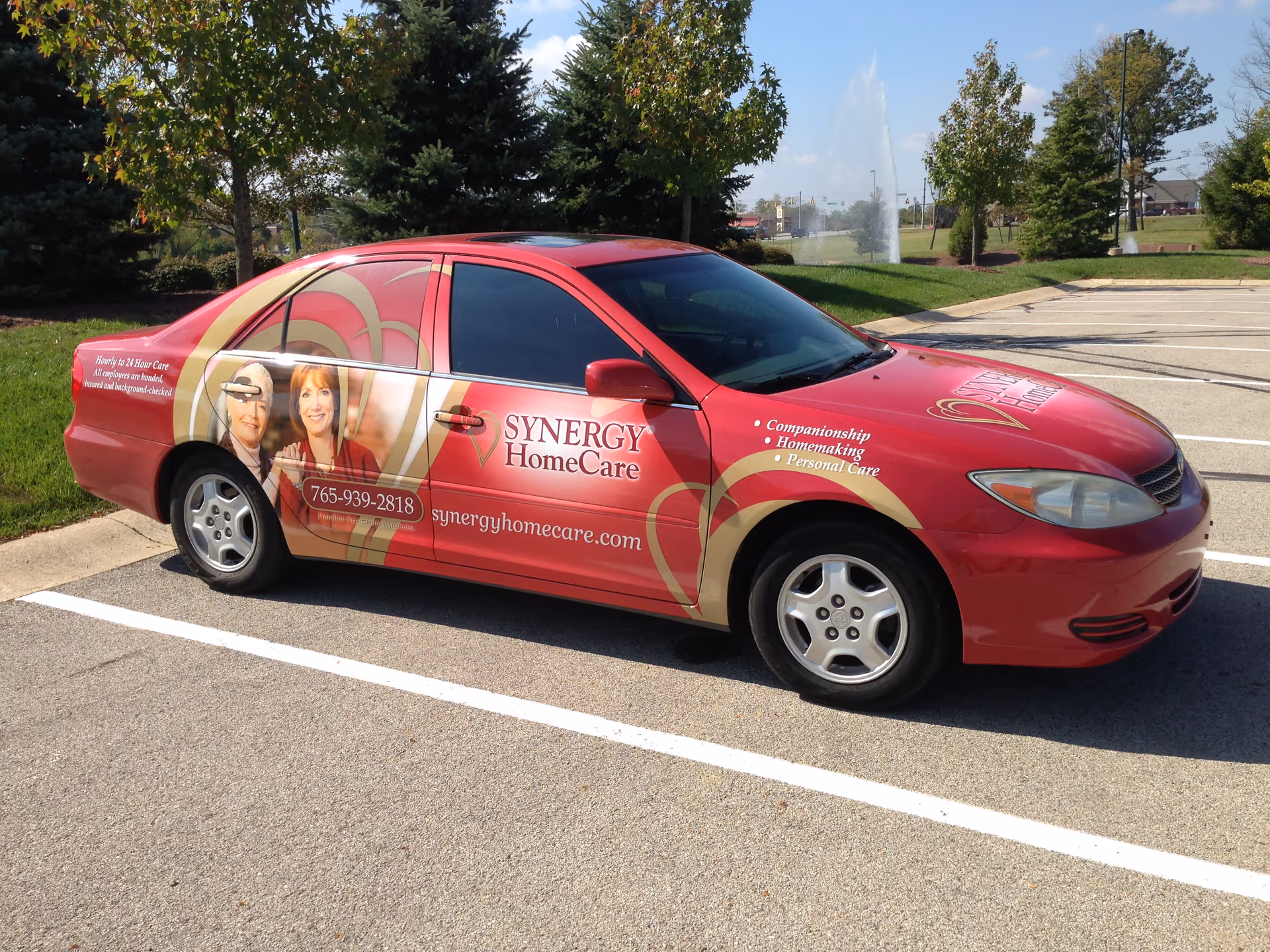 Red Synergy HomeCare promotional car with staff photos parked in a lot.