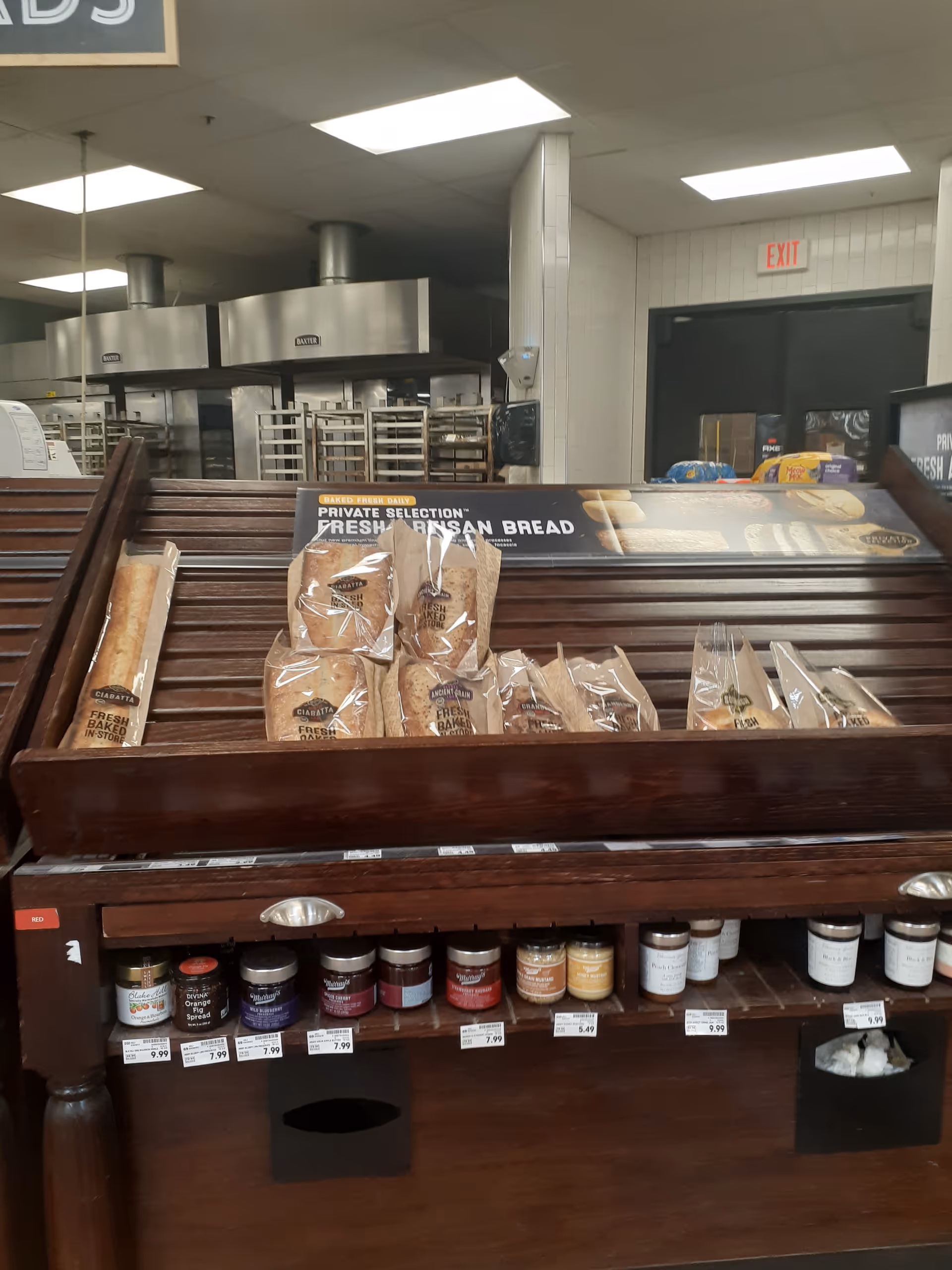 Wooden bread display with packaged loaves and stainless steel kitchen equipment behind.