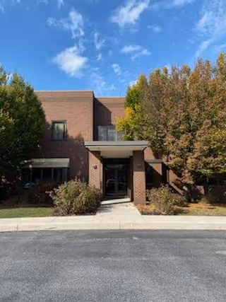 Brick hospice facility entrance framed by trees beneath a blue sky.