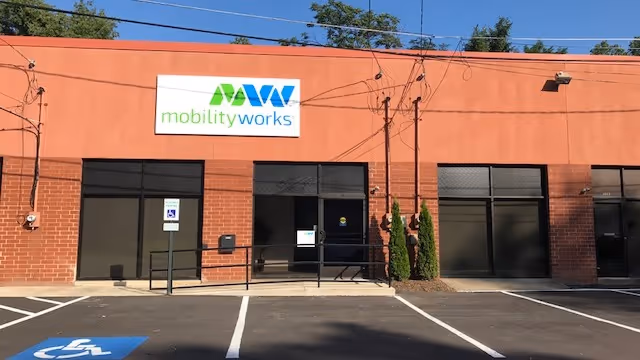 Orange-brick MobilityWorks building with sign, glass doors, and a parking lot in front.