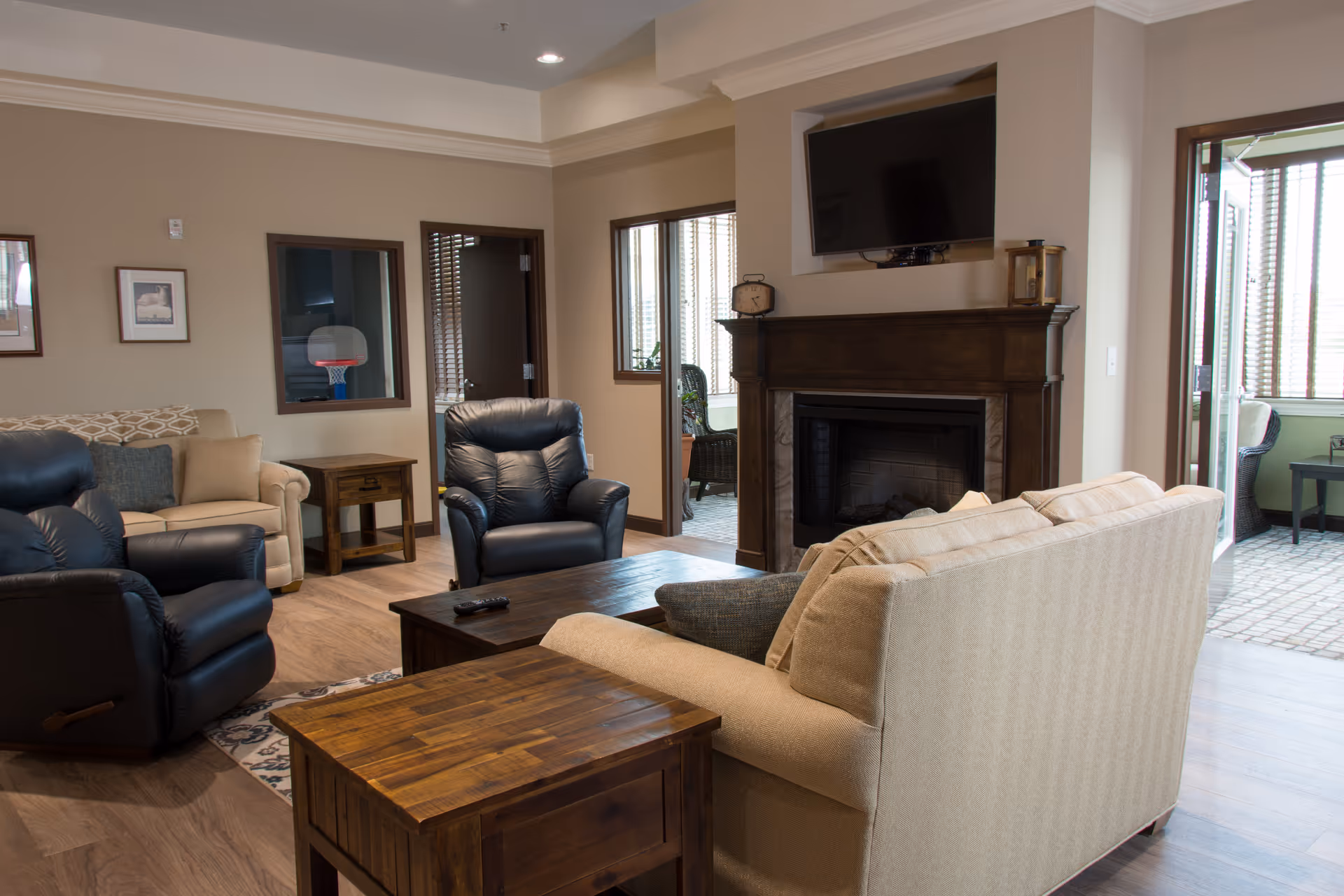 Cozy lounge with beige sofa, black recliners, coffee table, fireplace and mounted TV.