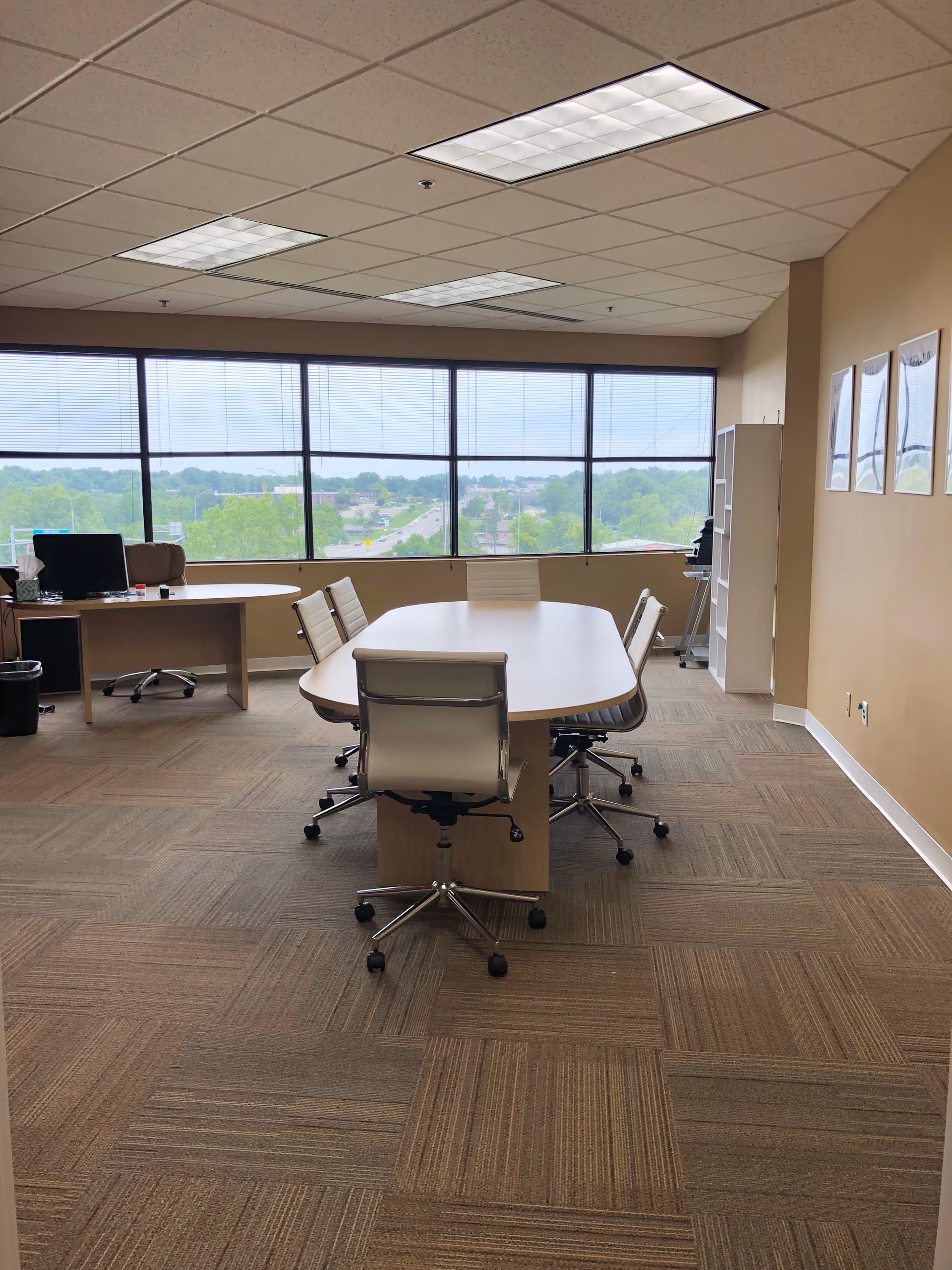 Interior meeting room with a curved table, chairs, and large windows overlooking trees.
