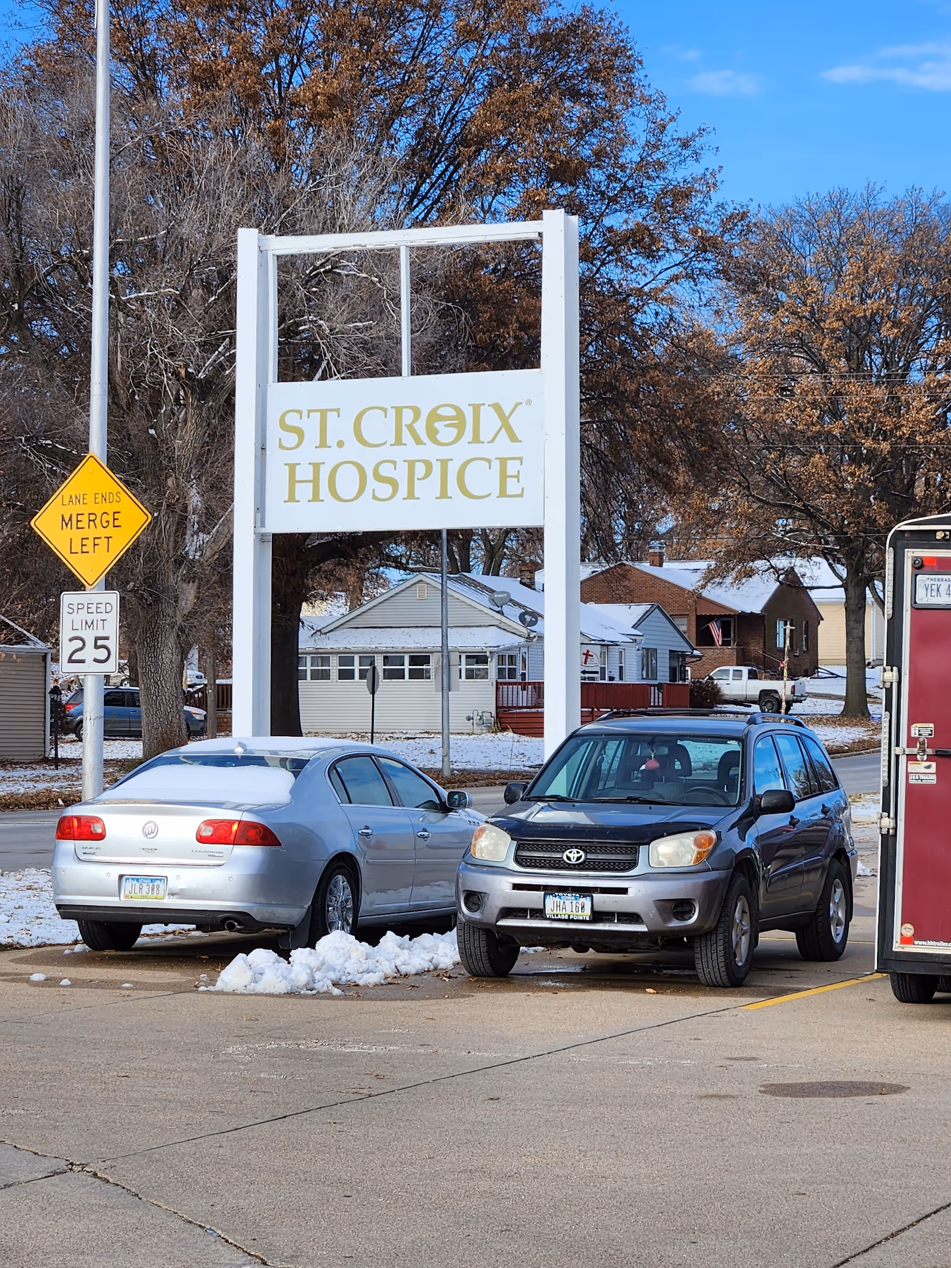 A St. Croix Hospice sign stands in a parking lot with cars and bare trees.