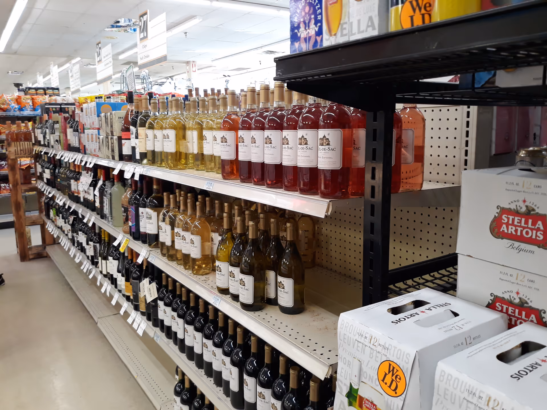 Aisle of wine bottles on shelves with beer boxes in a store.