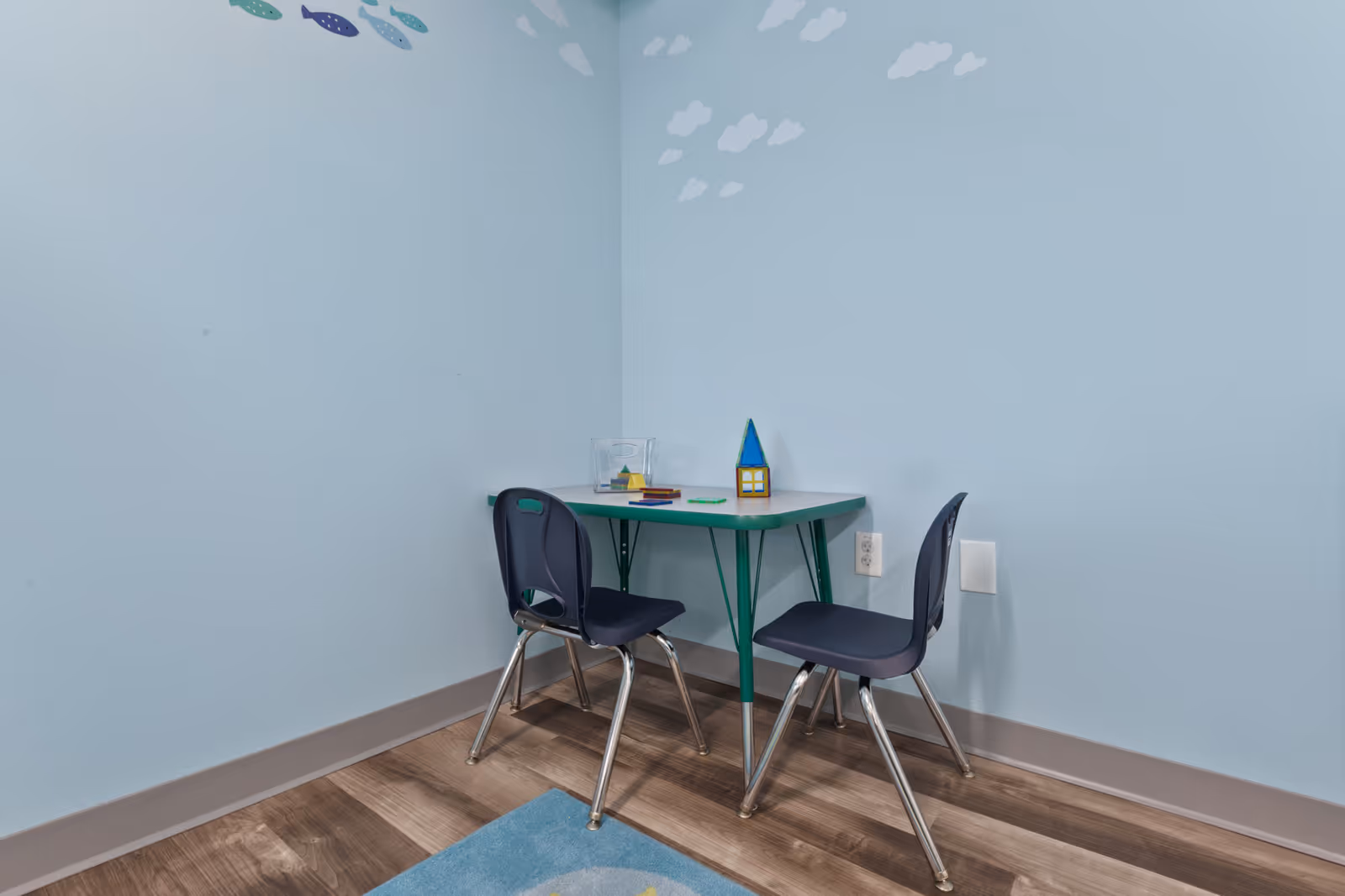 Small corner of a light blue room with a green table and two chairs.