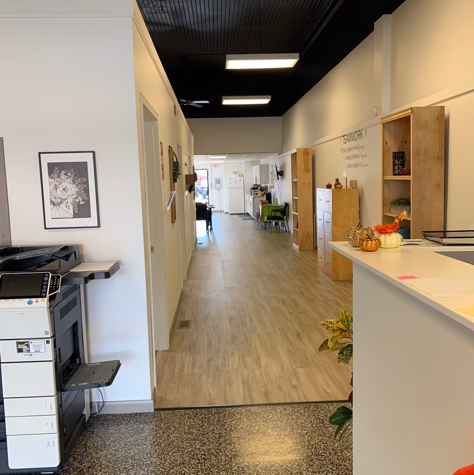 Long brightly lit interior hallway of a senior facility with a reception desk and cabinets.