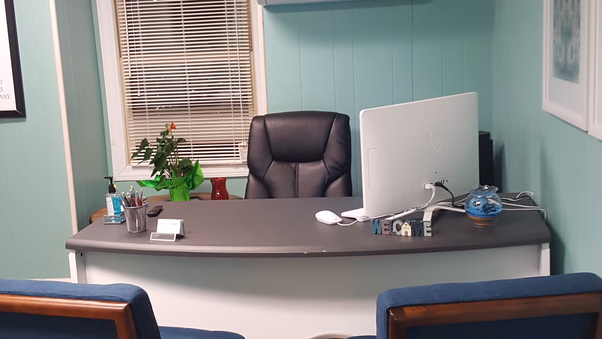 Reception desk with computer, plant, and waiting chairs in teal-walled interior