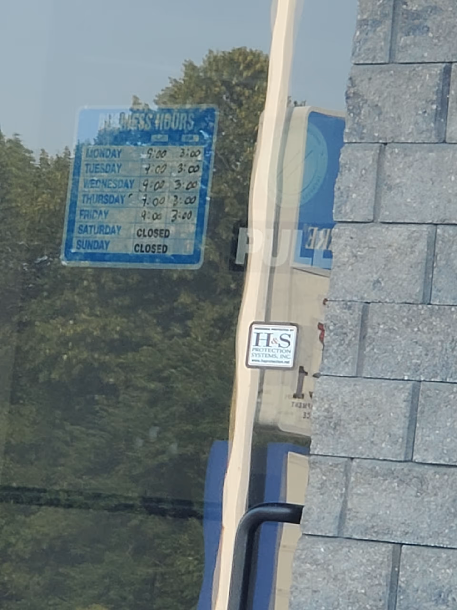 Exterior storefront with blue hours sign reflected in glass beside a stone wall