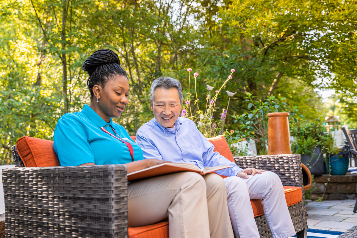 Two people sit on an outdoor wicker couch, looking at a binder together.