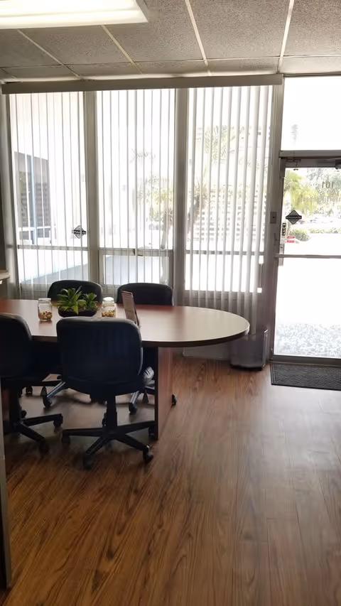 Interior room with a round table, office chairs, plants, and glass doors.