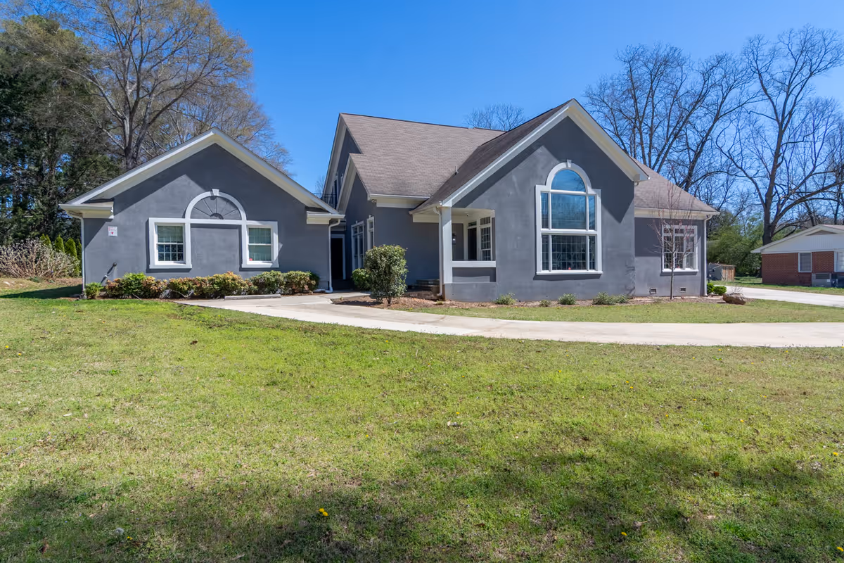 Gray, single-story building with arched windows and a curved driveway.
