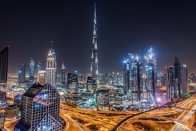 Nighttime city skyline with tall illuminated skyscrapers and elevated highways.