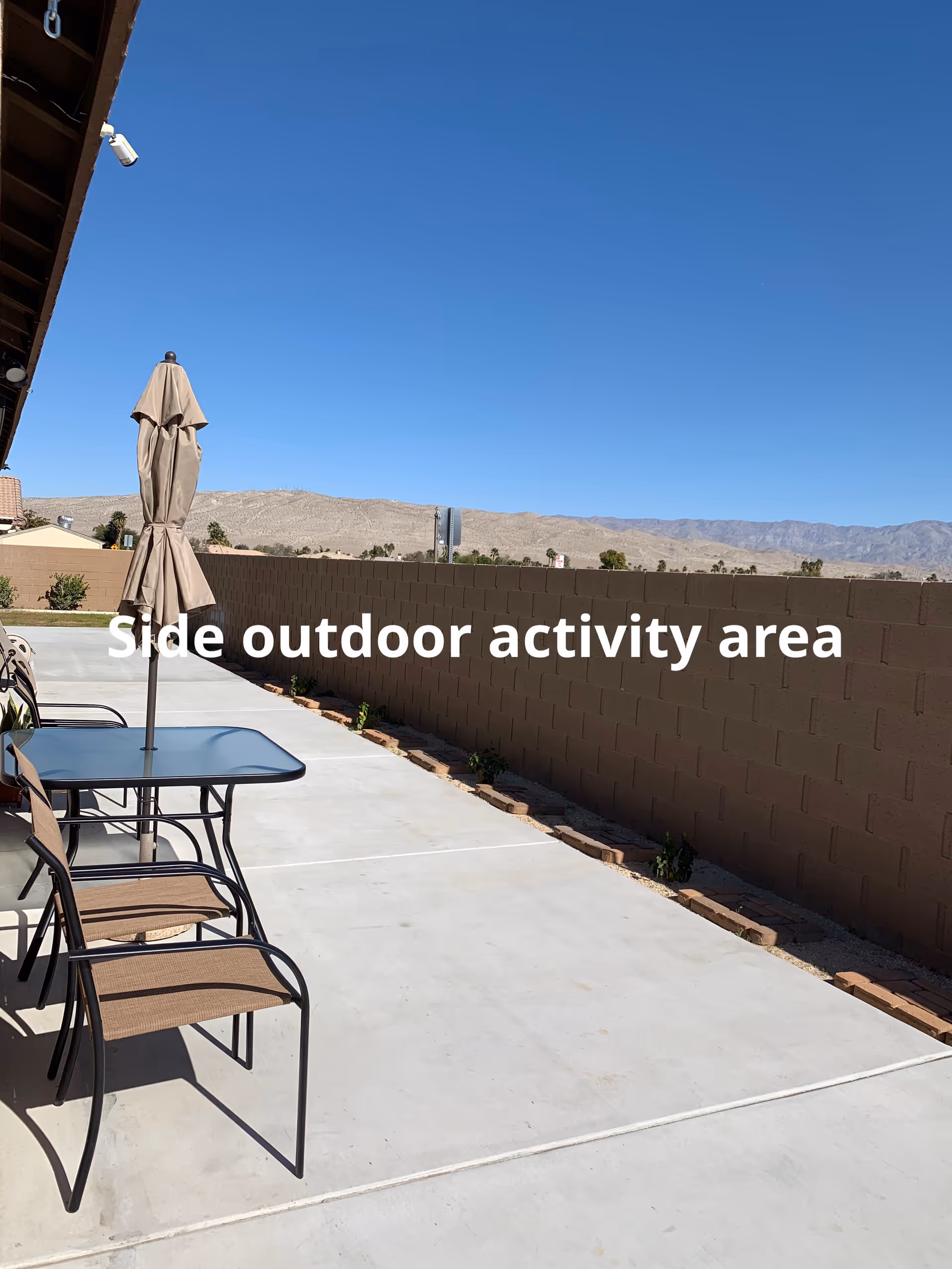 Outdoor patio with table, chairs, umbrella, and a brick privacy wall against desert mountains.