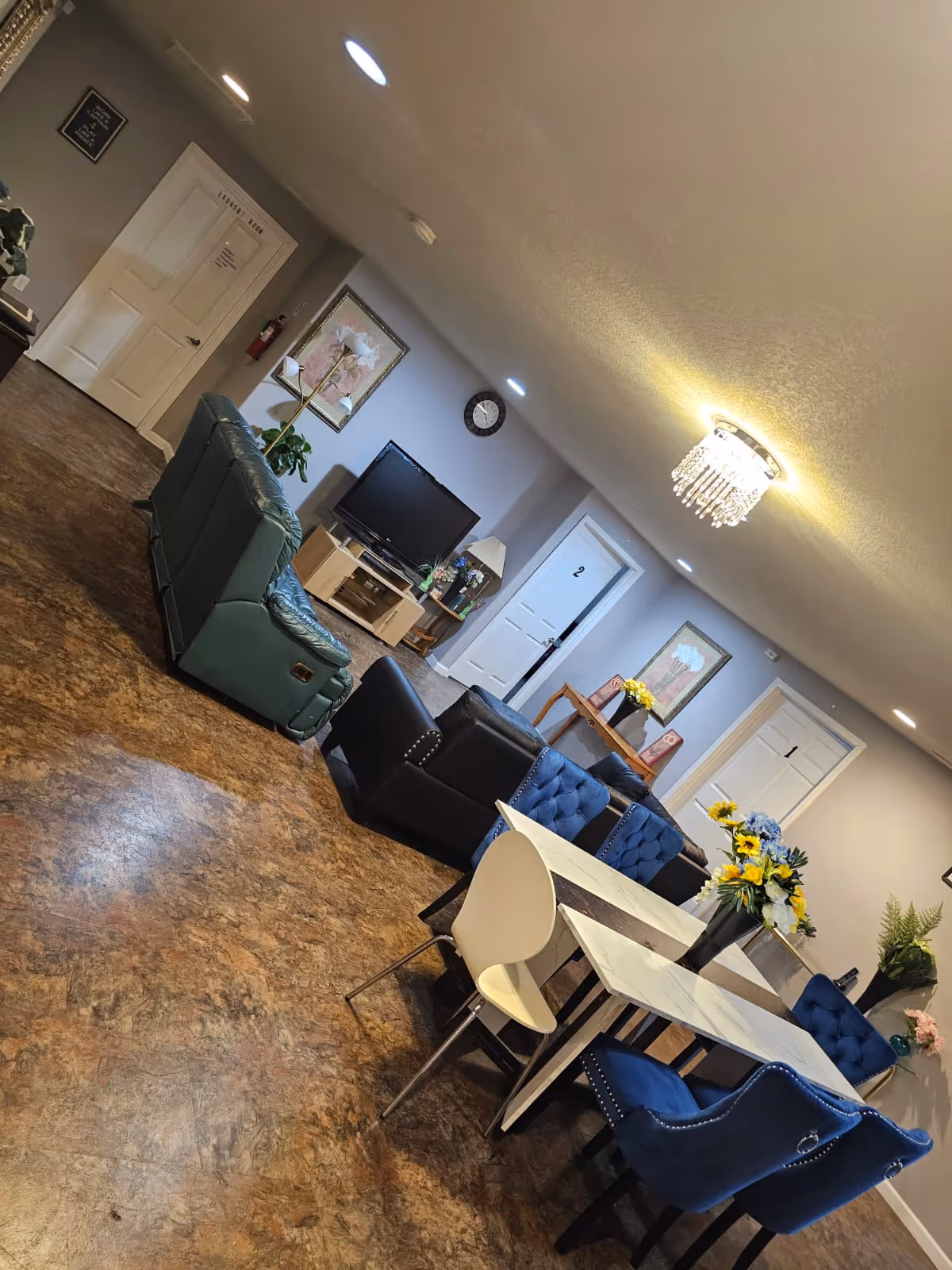 Senior living lounge with blue chairs, a green recliner, TV, and dining table.