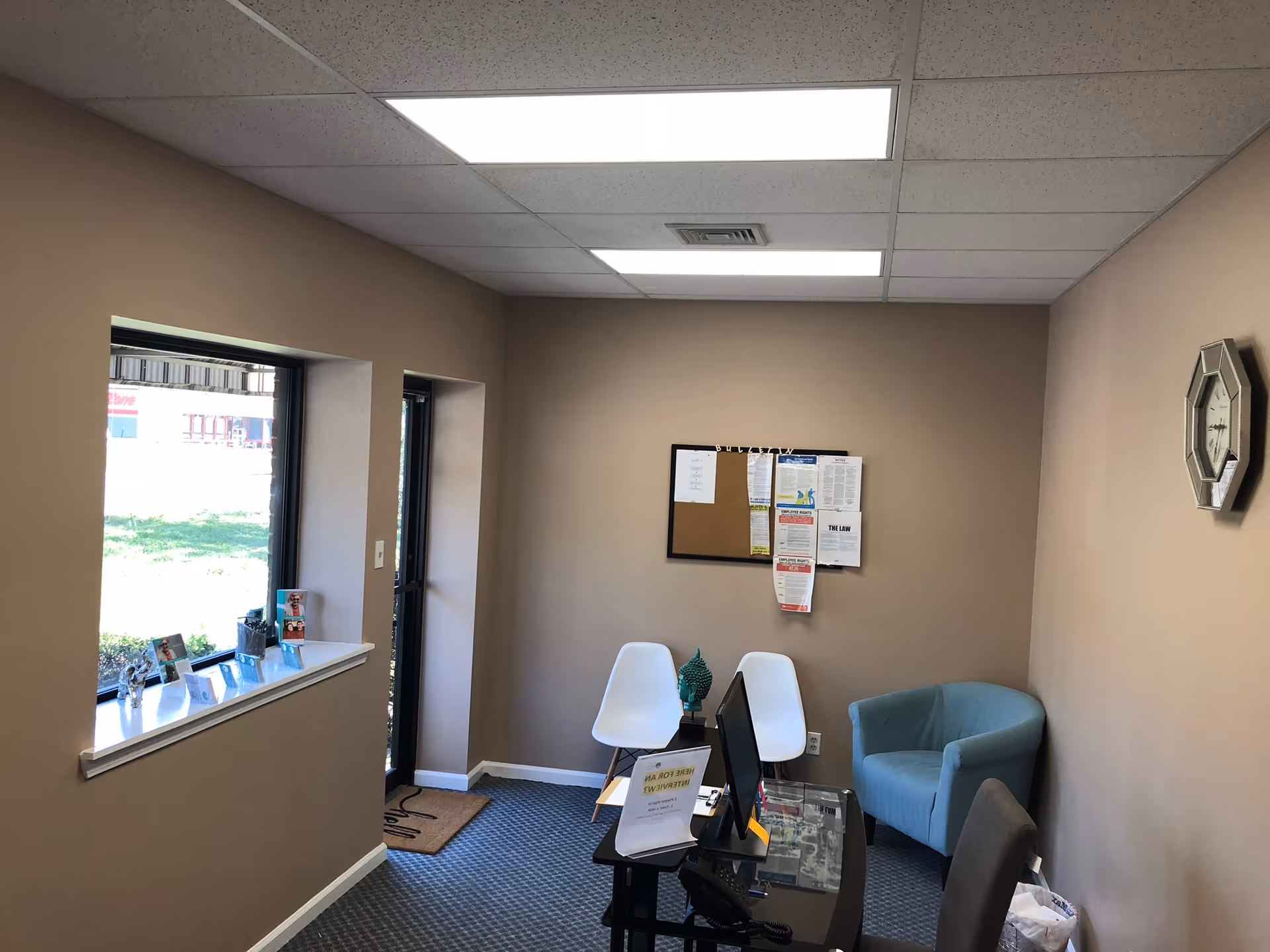 Reception area with desk, computer, chairs, bulletin board, and beige walls