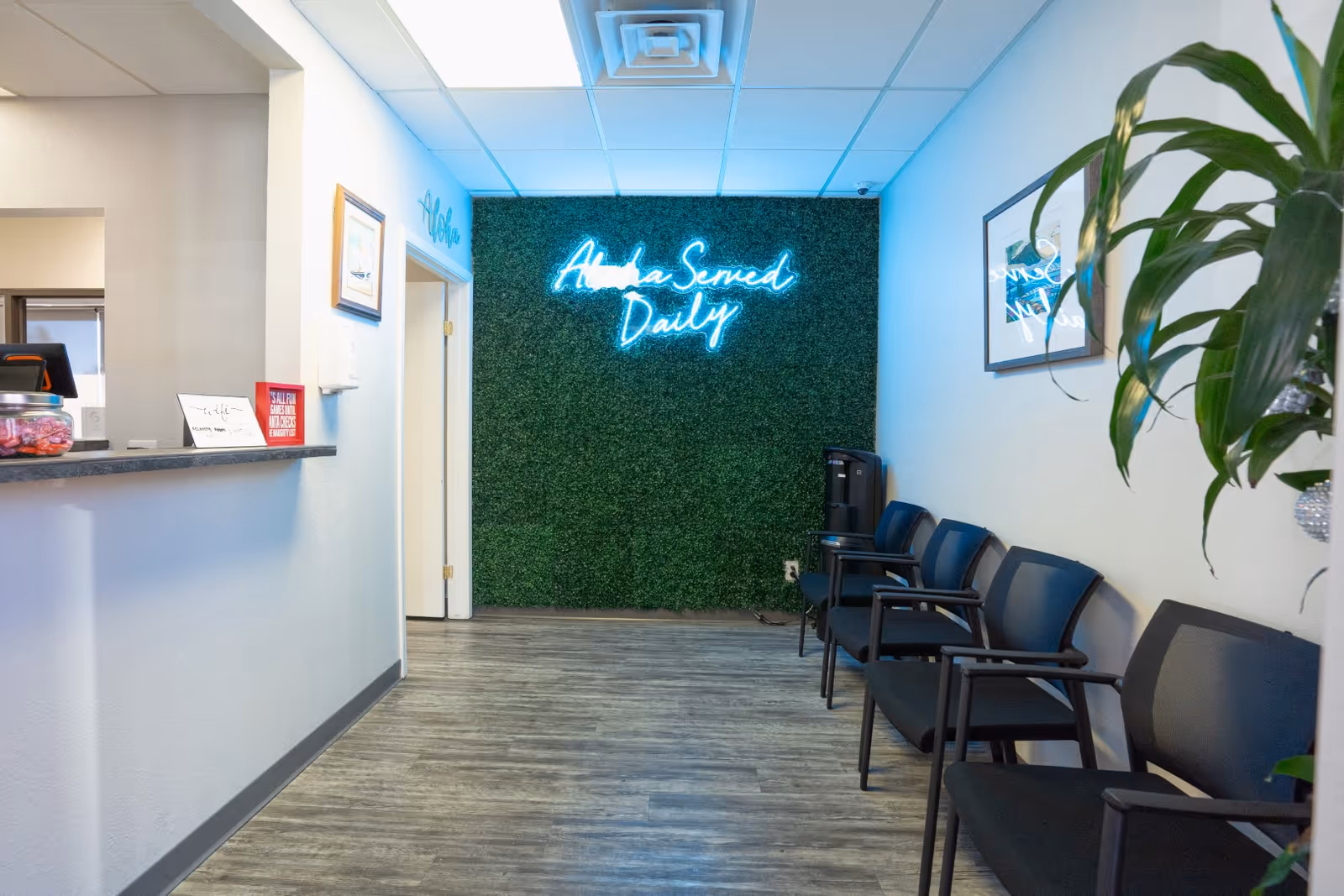 Reception area with neon sign on a green moss wall and chairs.