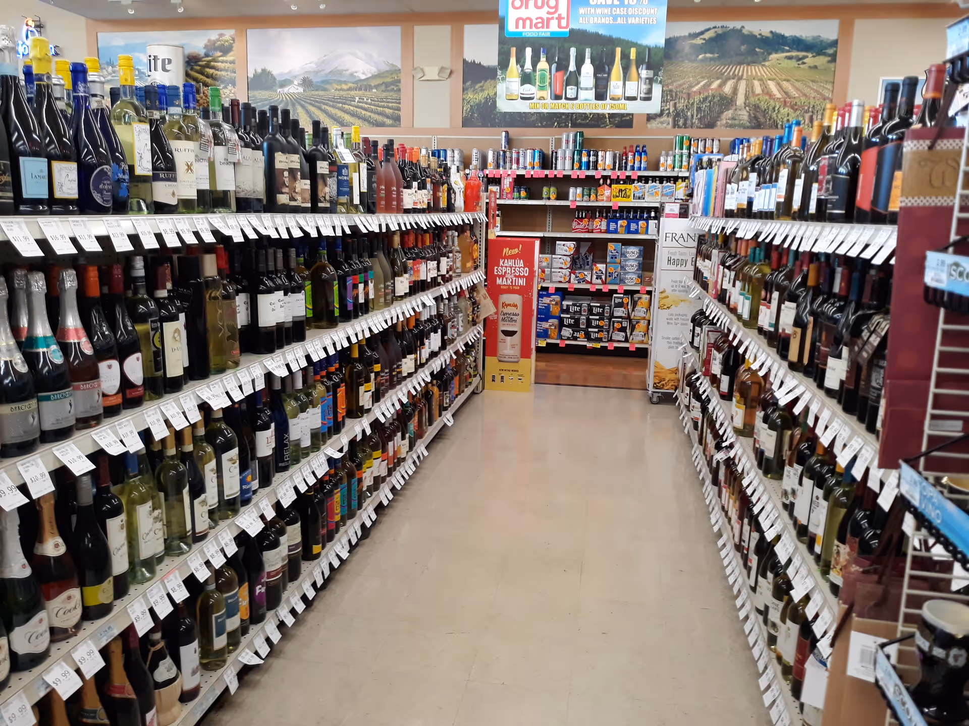 Aisle lined with wine bottles on shelves inside a Discount Drug Mart store.