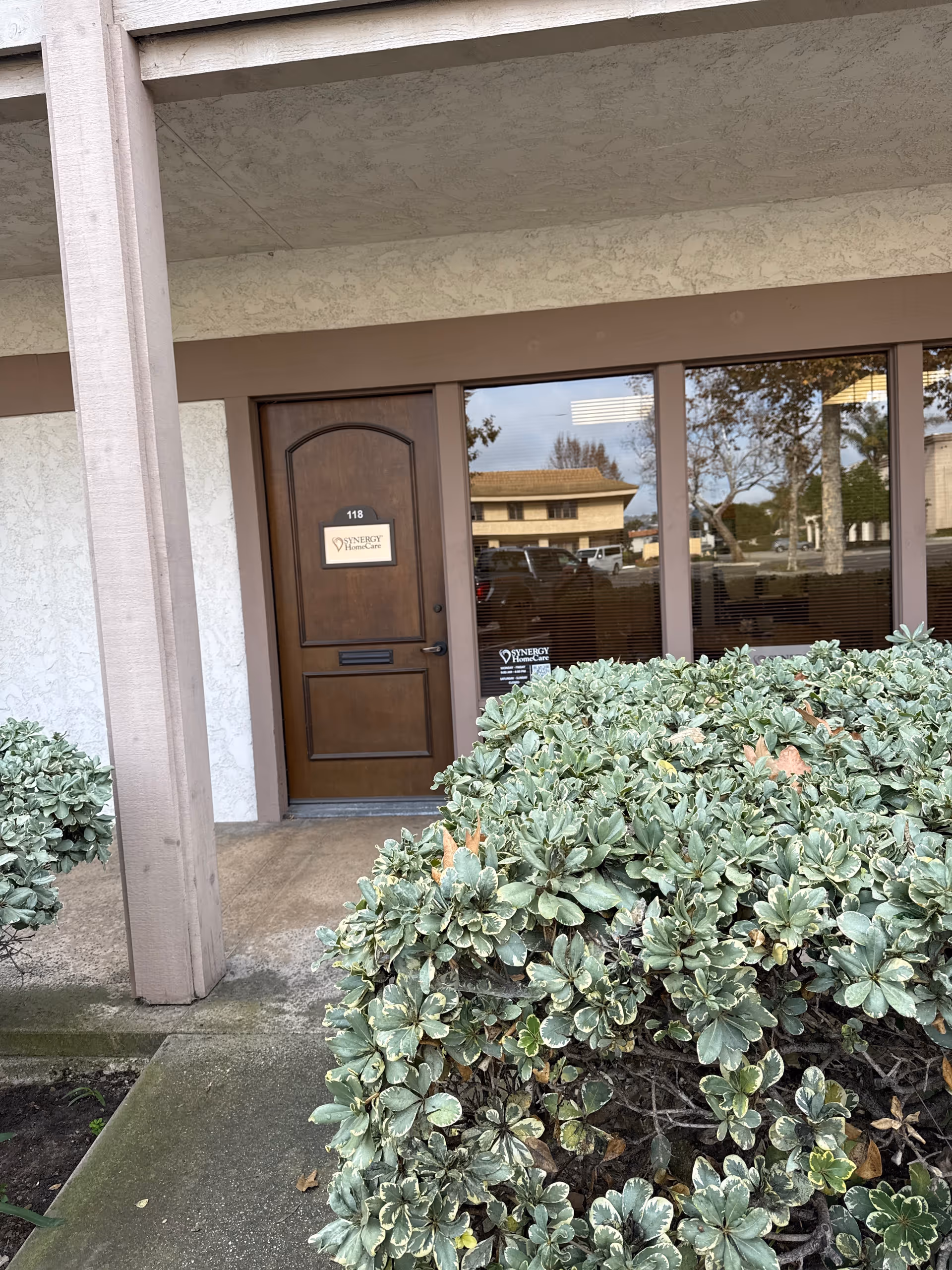 Front entrance of Synergy HomeCare with glass windows and trimmed shrubs.