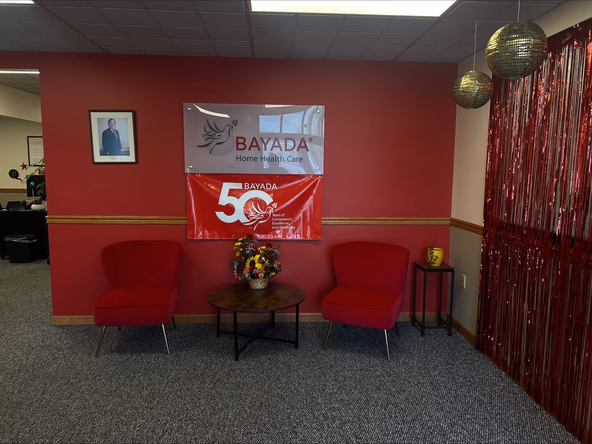Red-walled lobby area with two red chairs, a coffee table, and BAYADA banners.