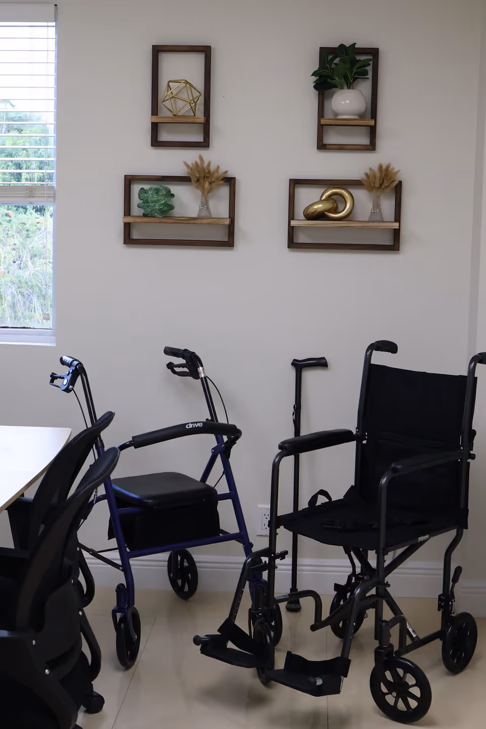 Wheelchairs and walkers near a wall with decorative shelves in a bright room.