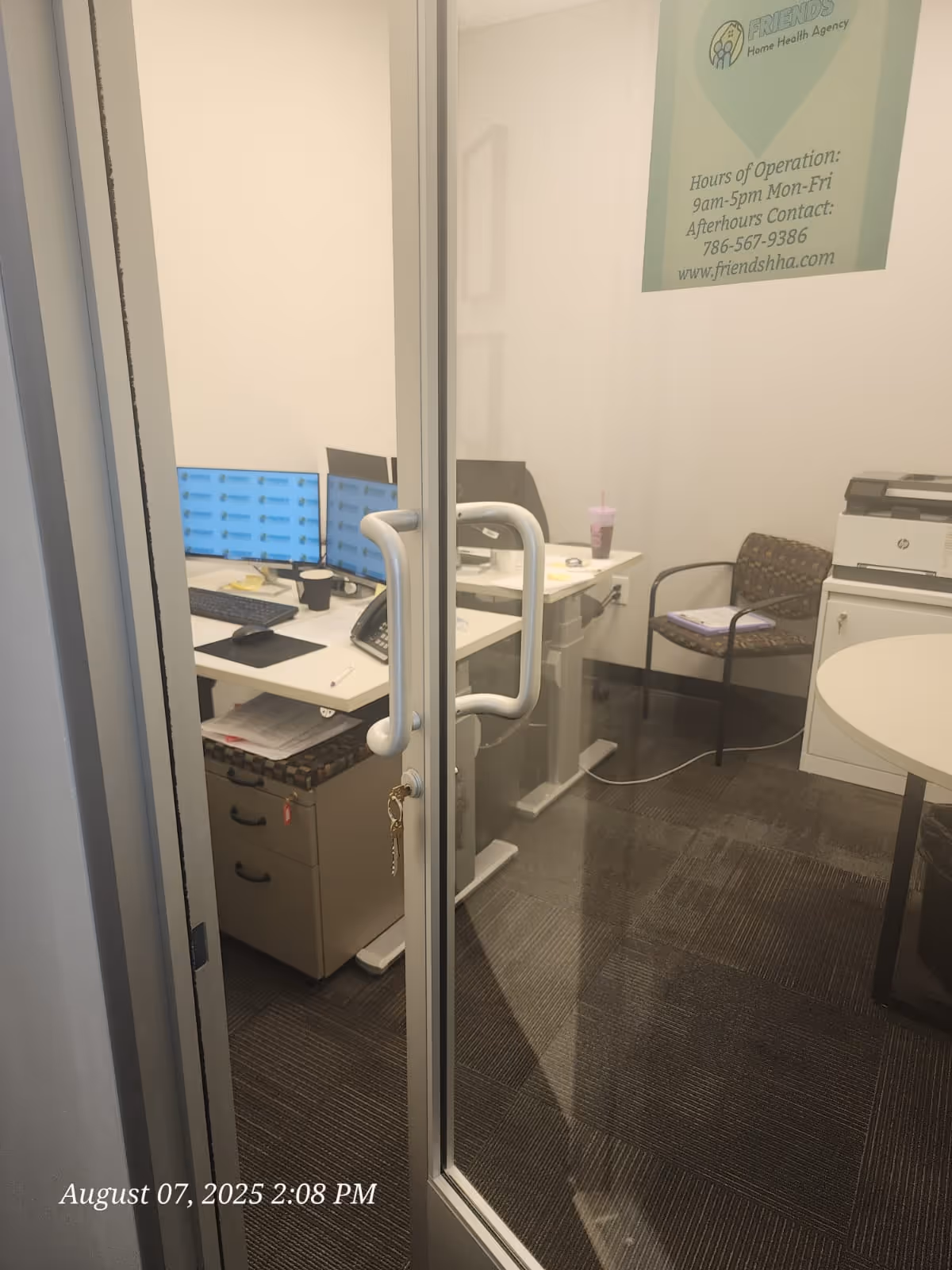 Glass door with handle opens to a small office workstation with computers and a printer.