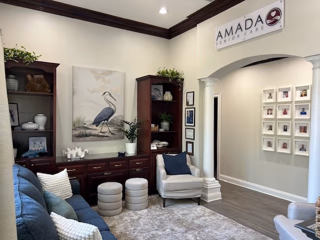 A welcoming Amada Senior Care lounge with couches, art, plants, and shelving.