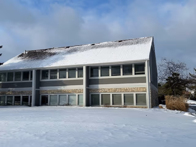 Two-story gray building with numerous windows in a snowy landscape, exterior view.