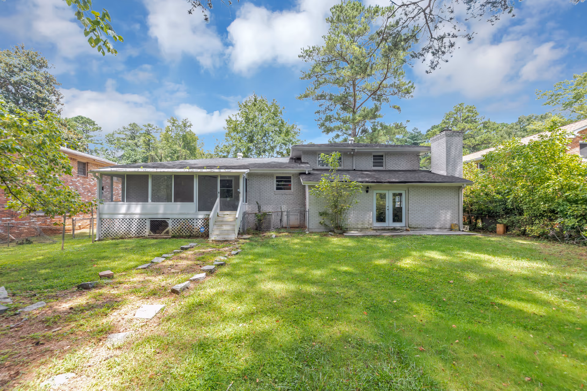 Backyard view of a single-story gray house with a screened porch and lawn.