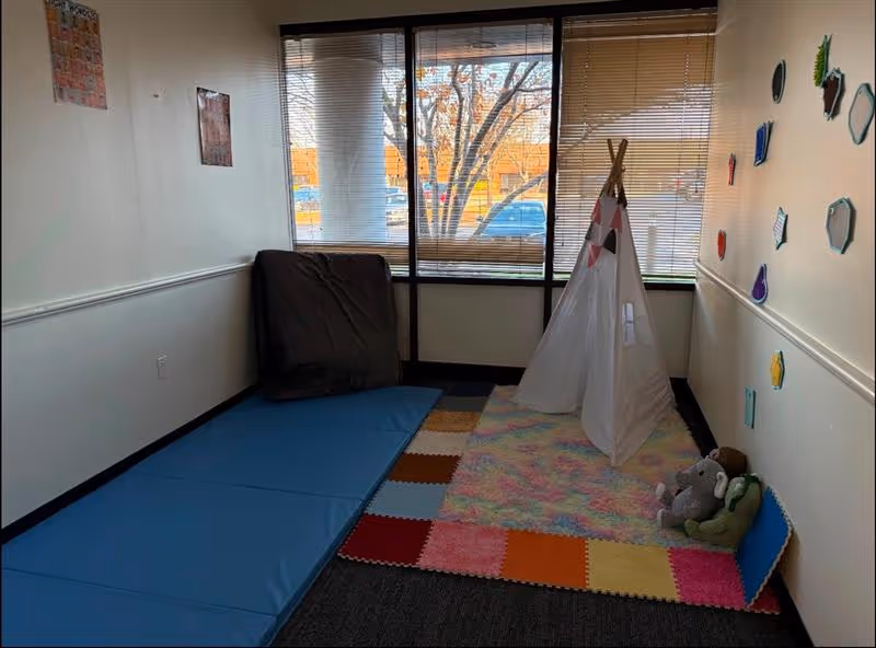 Small sensory play area with mats, a white fabric tent, and toys by a window.