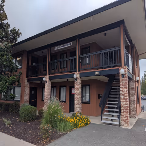Exterior view of a two-story Senior Helpers facility with brick pillars, balcony, and stairs.