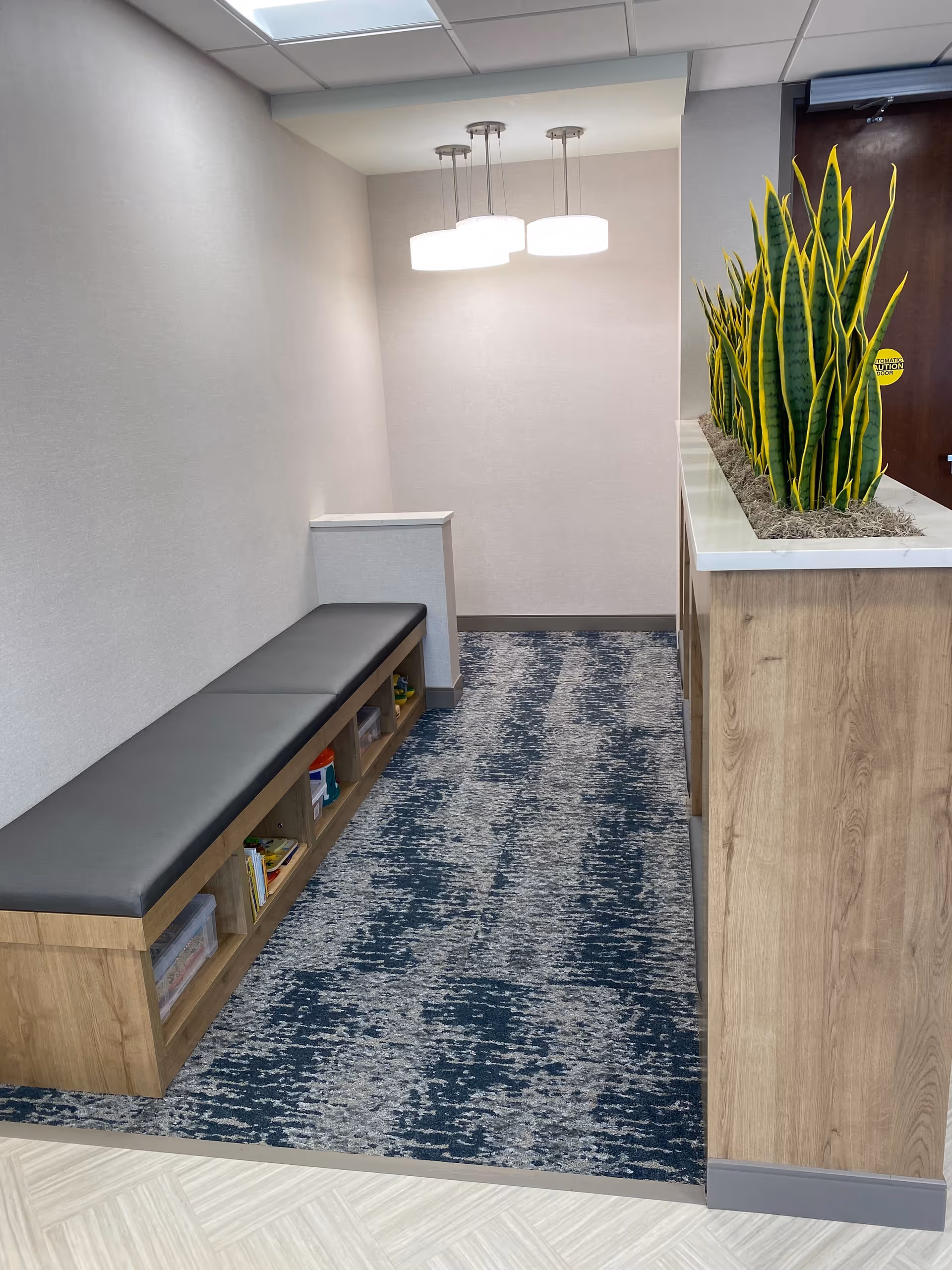 Narrow corridor with bench seating, cubbies, and a planter beside a wooden counter.