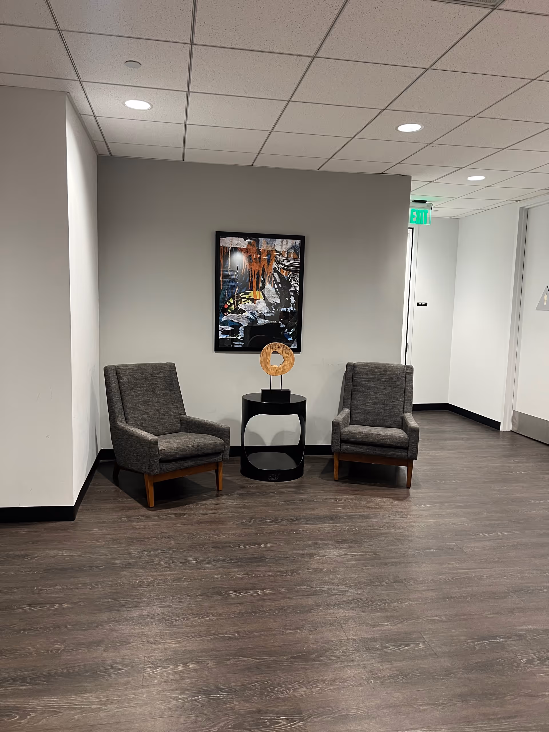 Lobby seating area with two gray armchairs, a small black table, and wall art.