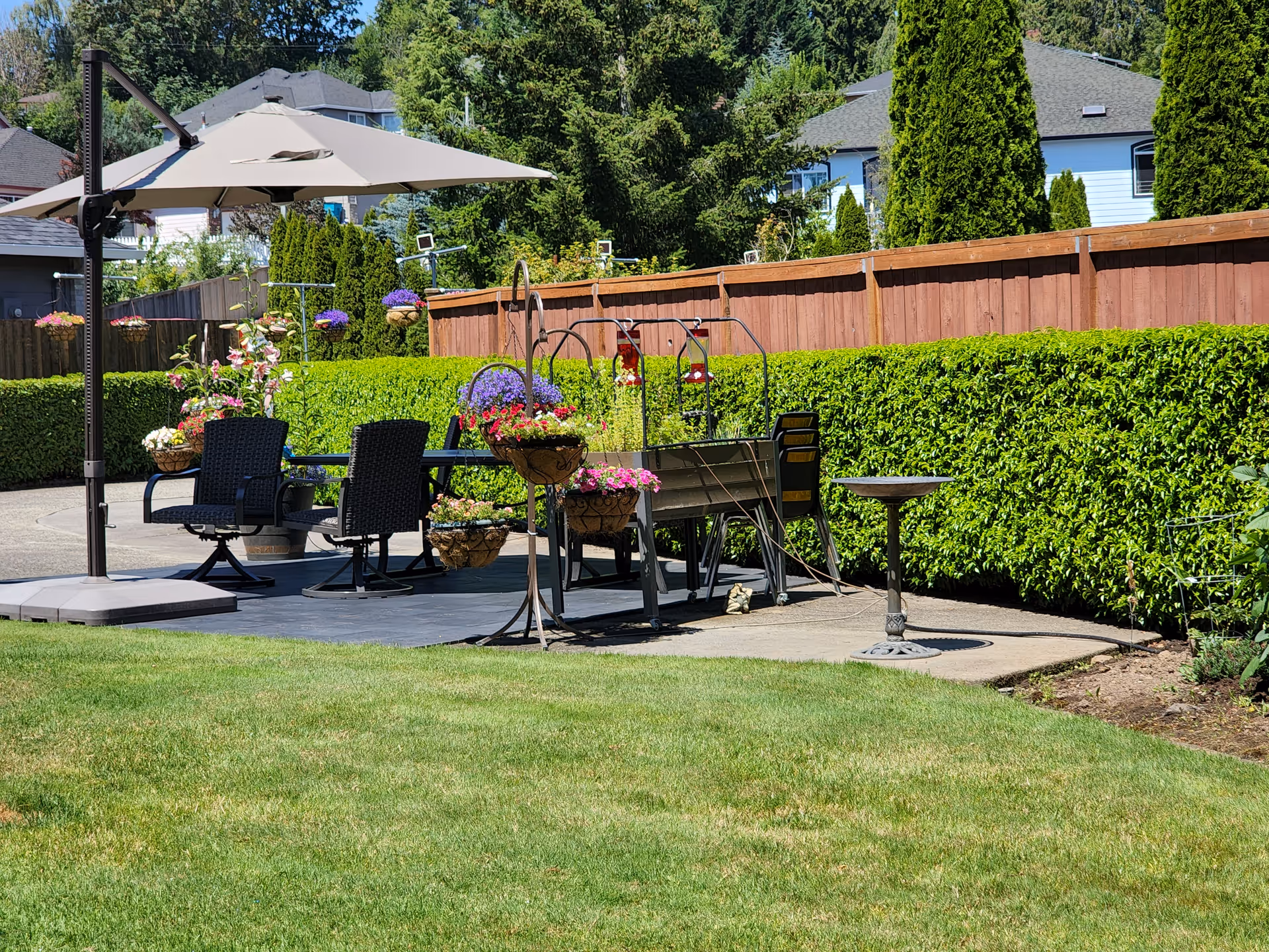 Outdoor patio with umbrella, seating, and potted flowers along a wooden fence.