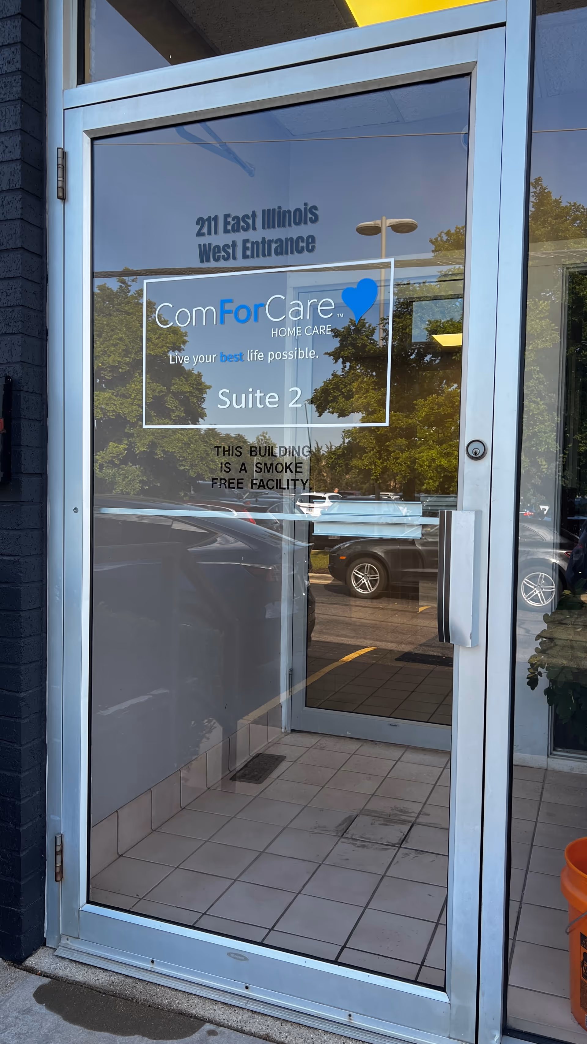 Glass door entrance to ComForCare Home Care suite with signage and reflections.
