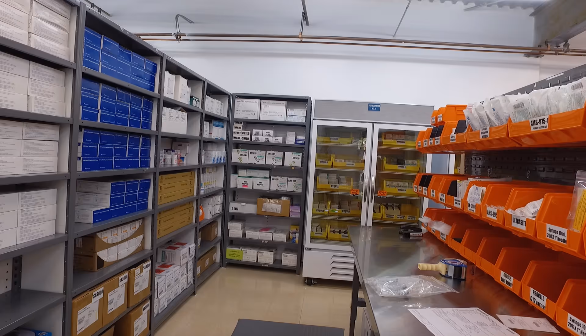 Medical supply storage room with metal shelves, boxes, and orange bins.