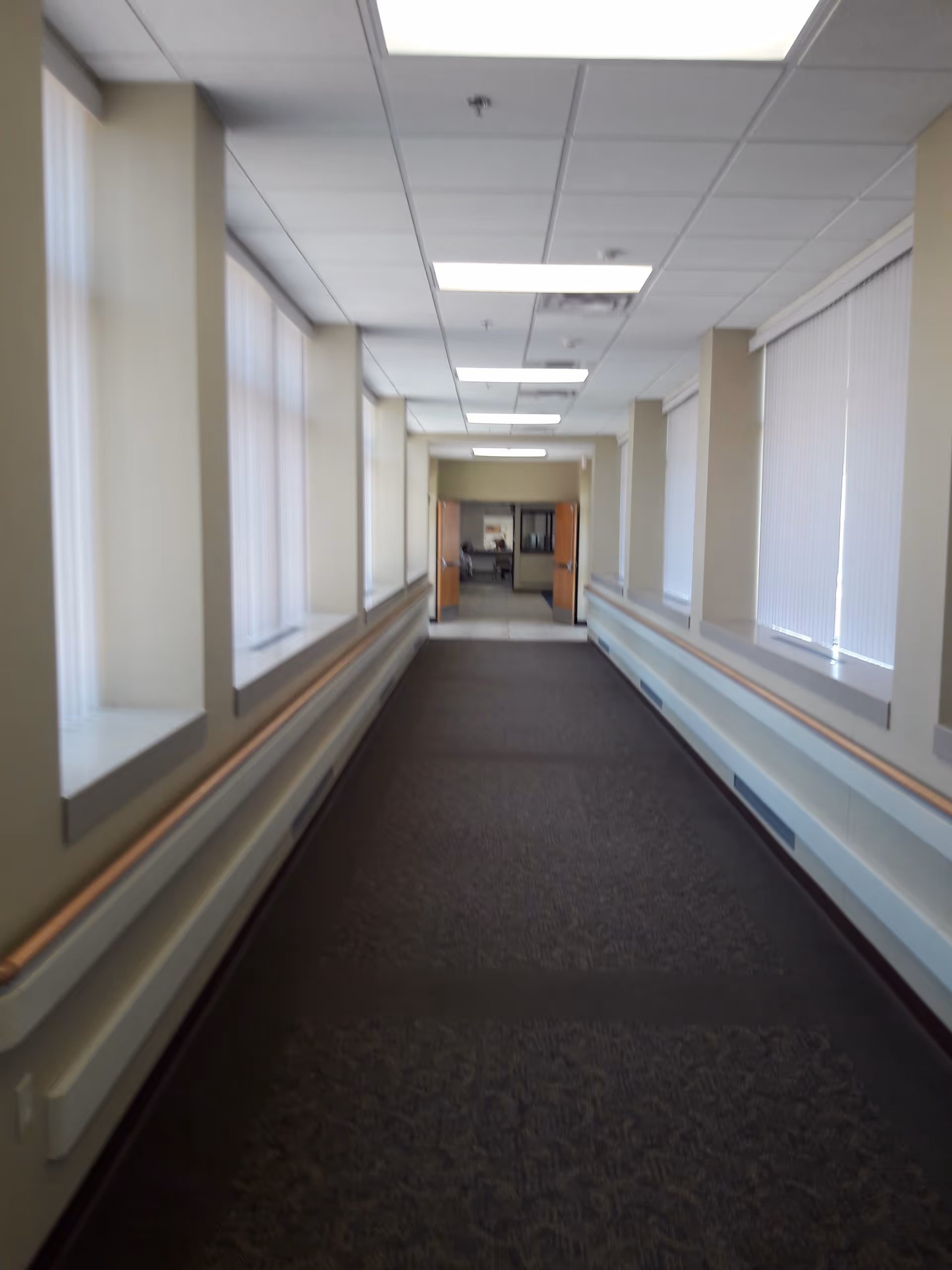 Long, well-lit interior corridor with windows on both sides and a door at the end.