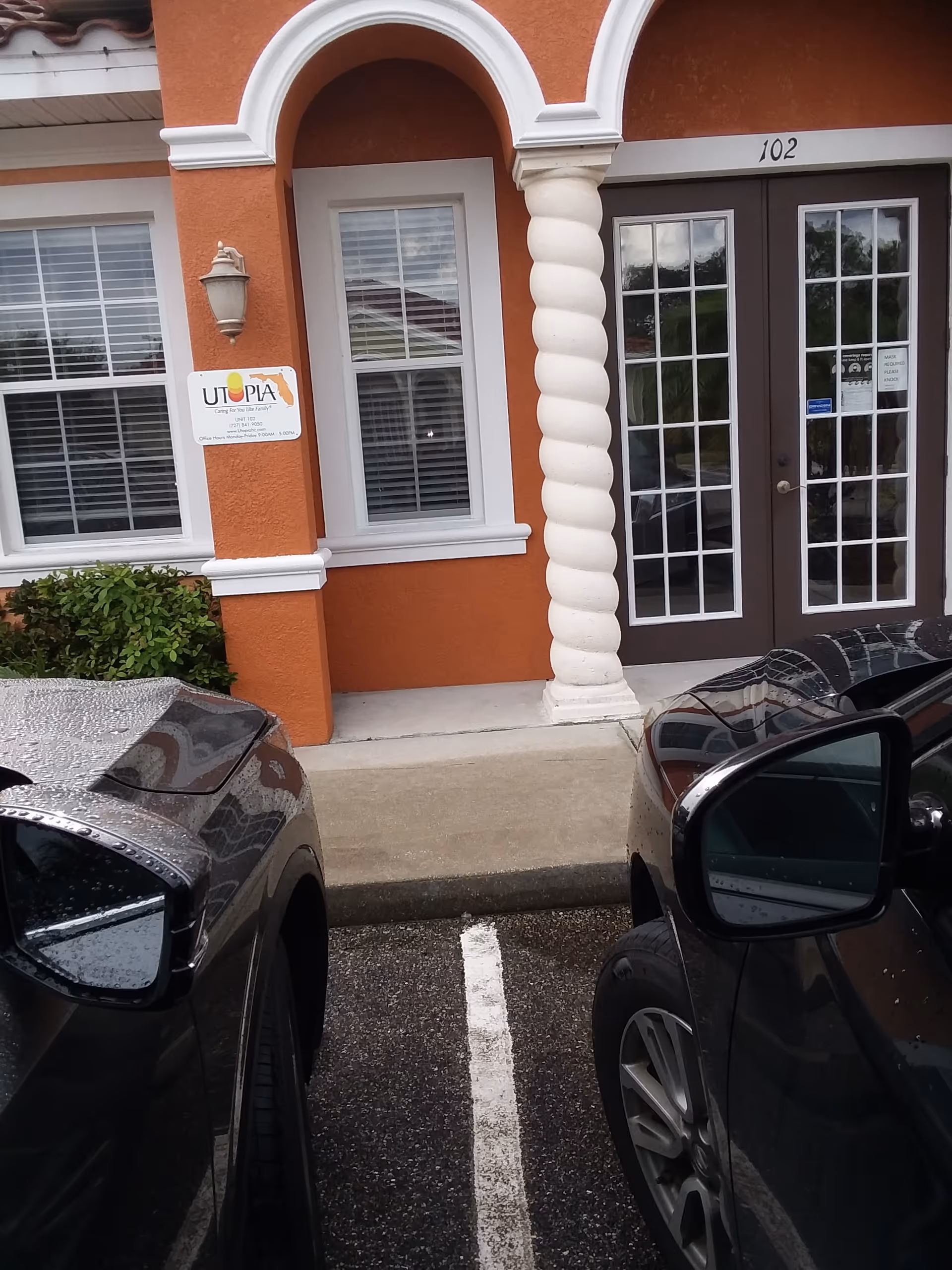 Front exterior of Utopia Home Care, Inc. building with arched entrance and parked cars.