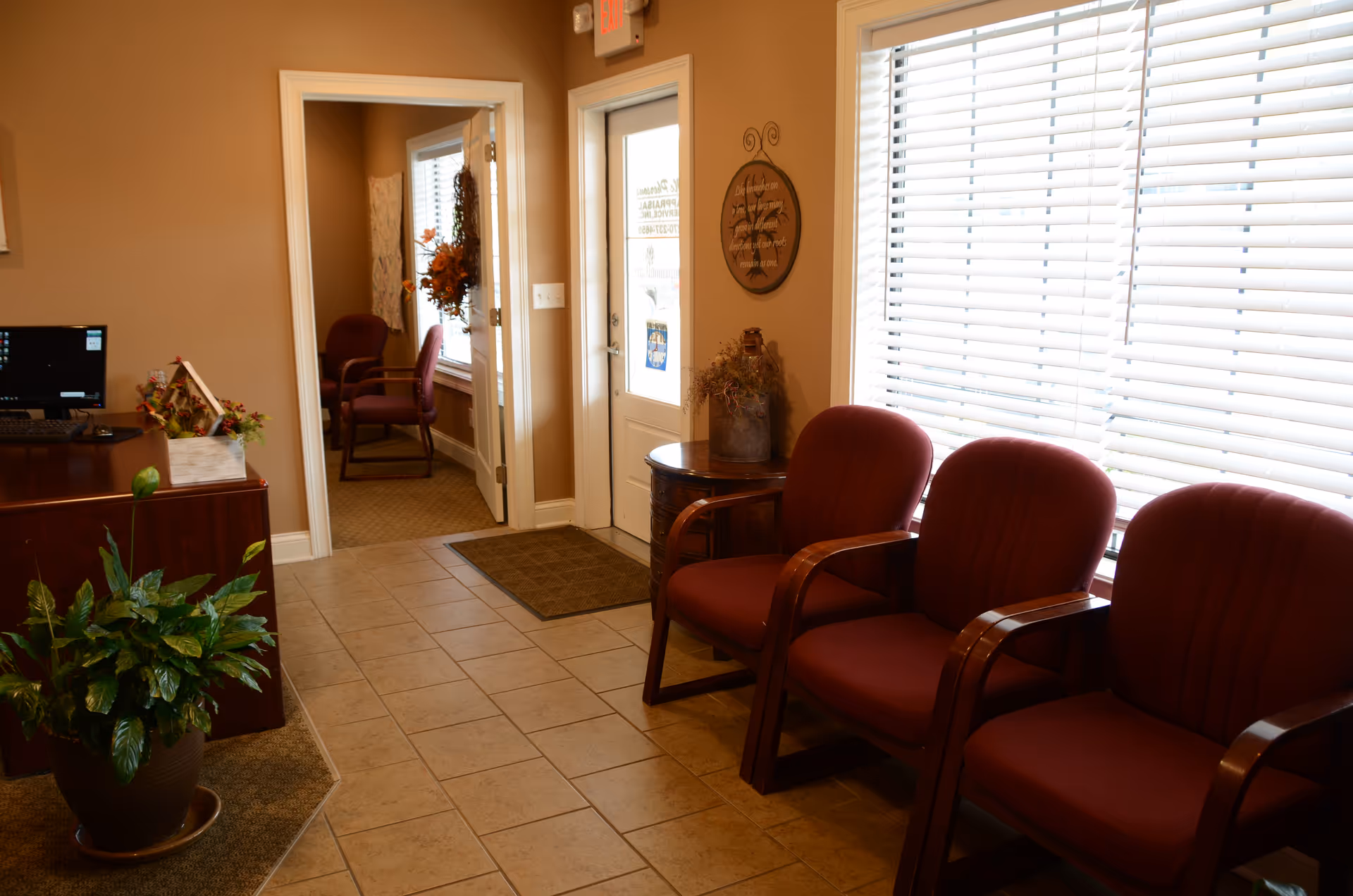 Waiting area with red chairs, blinds, a desk, plants, and doorway