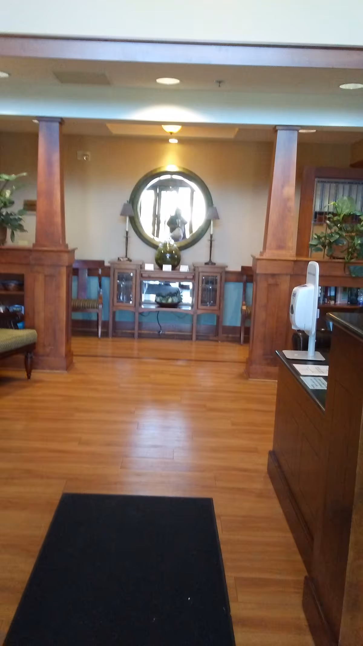 Wood-floored lobby with round mirror, console table, lamps, and seating area.